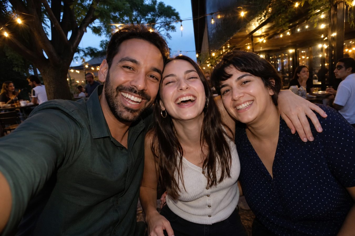 Three friends laughing in a group selfie at an outdoor cafe